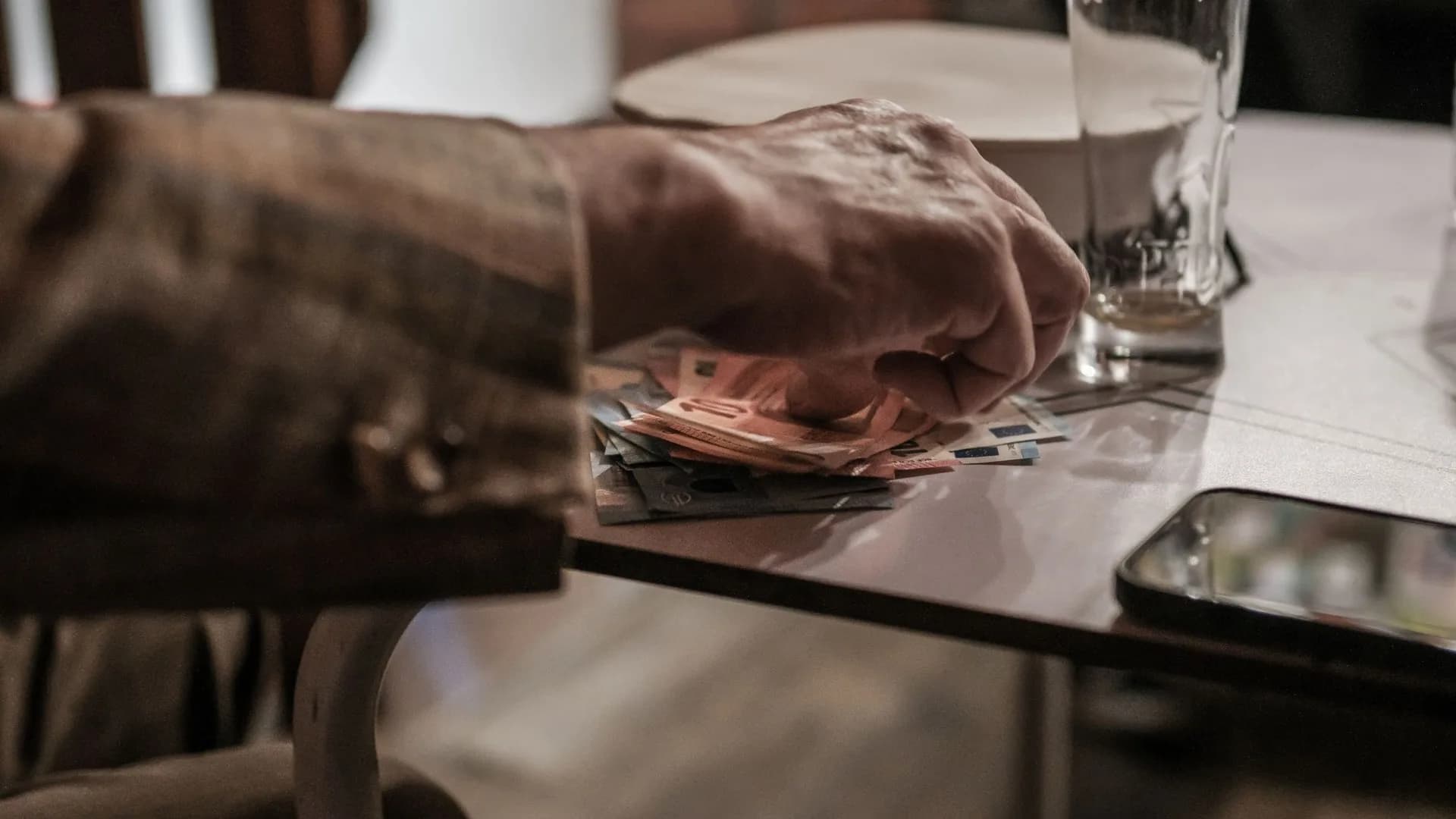 Dłoń licząca banknoty euro na stole obok telefonu